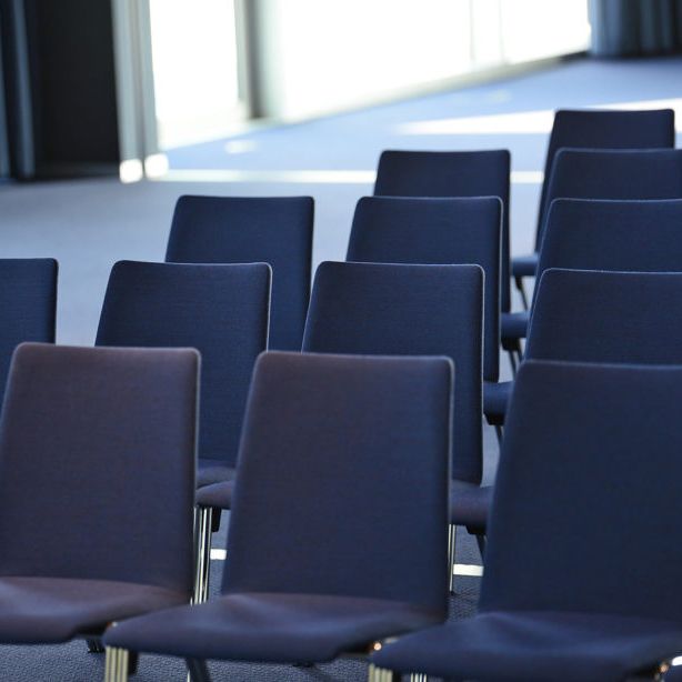 Dunkle Stühle, die ordentlich hintereinander aufgereiht sind.