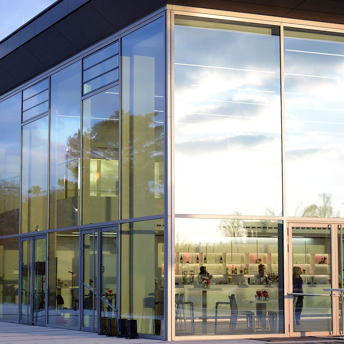 Moderne Glasfassade eines Gebäudes mit sichtbarer Bar und Menschen drinnen.