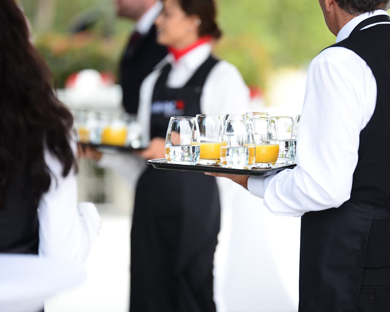 Nahaufnahme von Servicepersonal, das Tabletts mit orangen Getränken trägt.