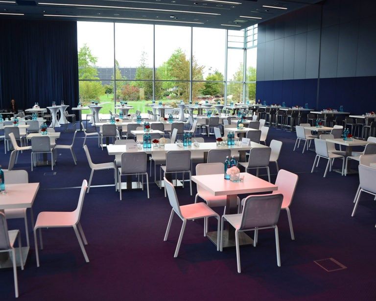 Großer Raum, mit weißen Tischen und Stühlen und Wasserflaschen auf jedem Tisch