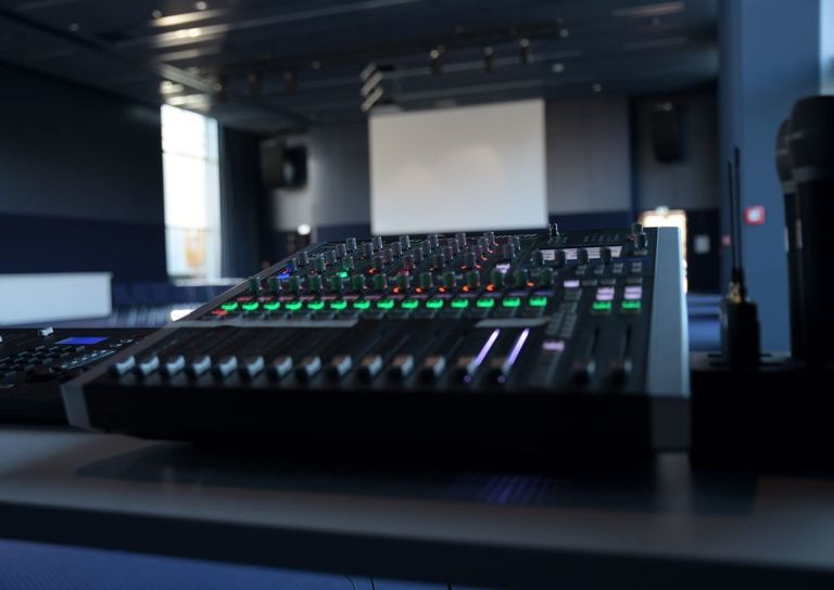 Nahaufnahme eines Mischpults und eine Leinwand im Hintergrund